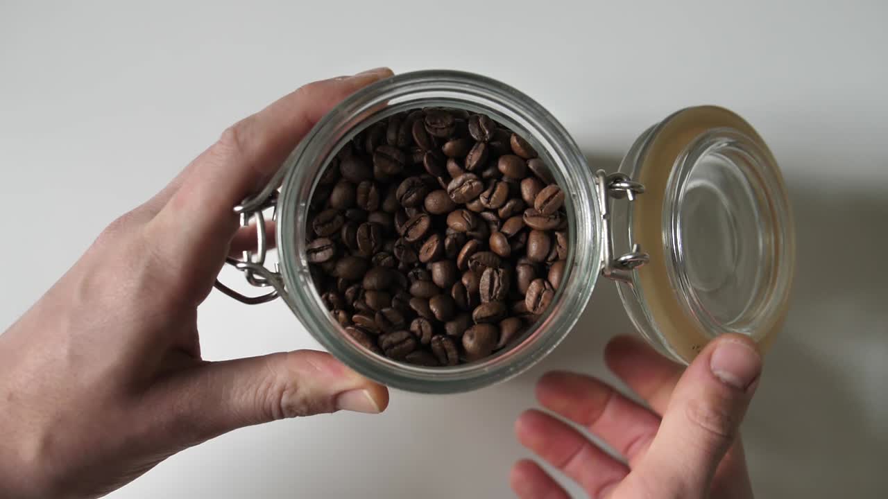 Close-up view of hands holding a glass jar filled with roasted coffee beans