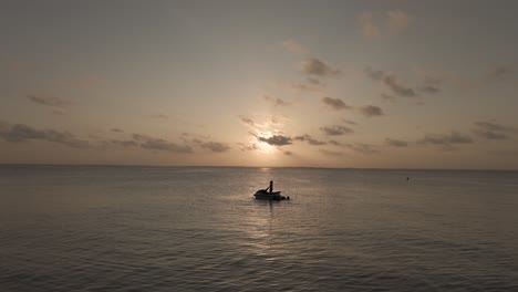 persona en un círculo de aviones no tripulados en silueta de jet ski en una suave puesta de sol suave con horizonte oceánico