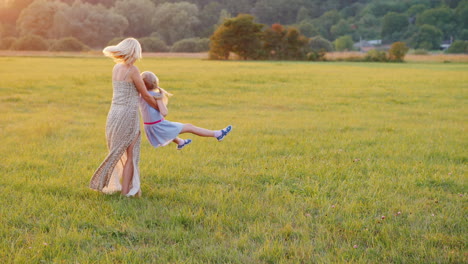 mom plays with her daughter twists her around her on a beautiful meadow at sunset active lifestyle 4