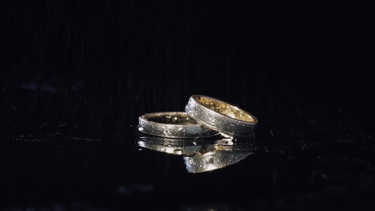 Wedding rings on dark water surface shining with light. Close up macro
