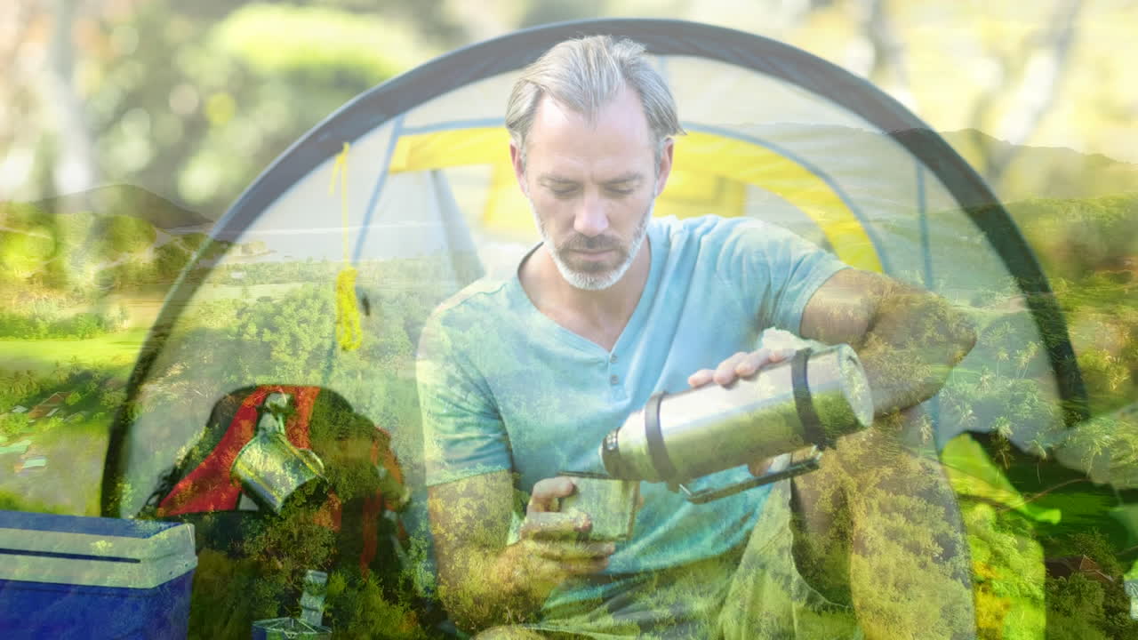 выливая напиток из термоса, человек лагерирует над живописным ландшафтом