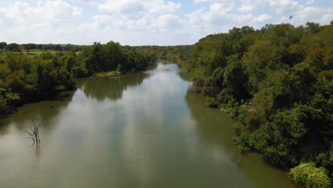 Aerial-view-of-river-next-to-sports-field,-sky-reflects-in-creek-water,-drone-4K