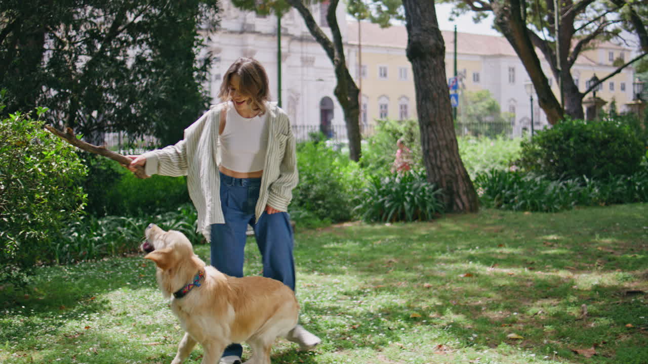 Happy girl training retriever in sunny garden. Dog catching stick having fun