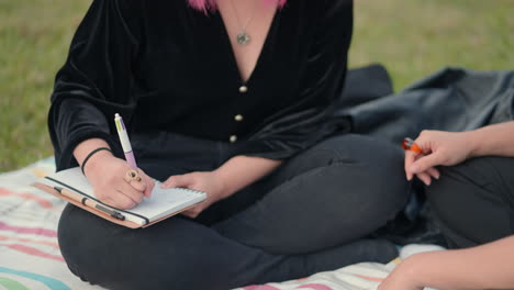 two women having a conversation and writing in a park