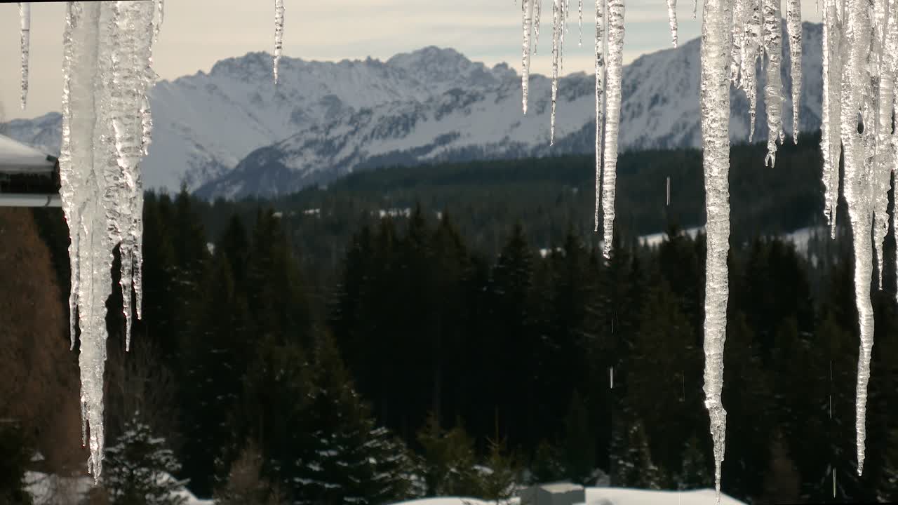 hielo en el techo derritiéndose en el sol contra el telón de fondo de montañas nevadas y bosque