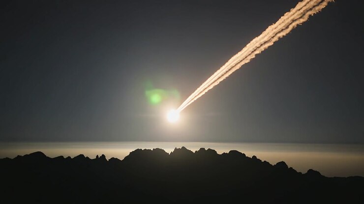 Appearing meteor entering air, making twin trail, moving over foggy ridge at night, shedding sparks