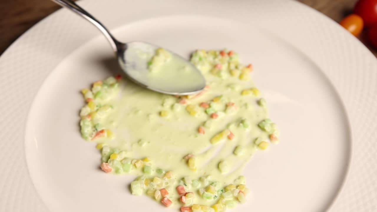 Chef che impiattano verdure a cubetti con salsa verde su un piatto bianco