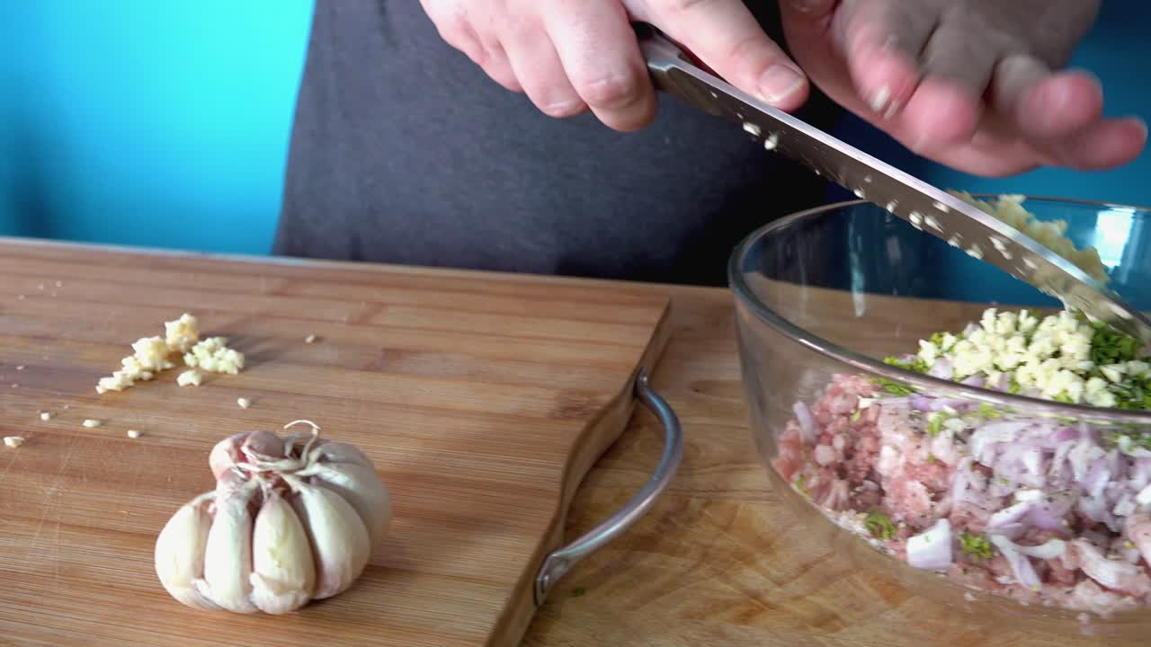 Aggiunta di aglio fresco tritato all'impasto delle polpette su un tagliere di legno.