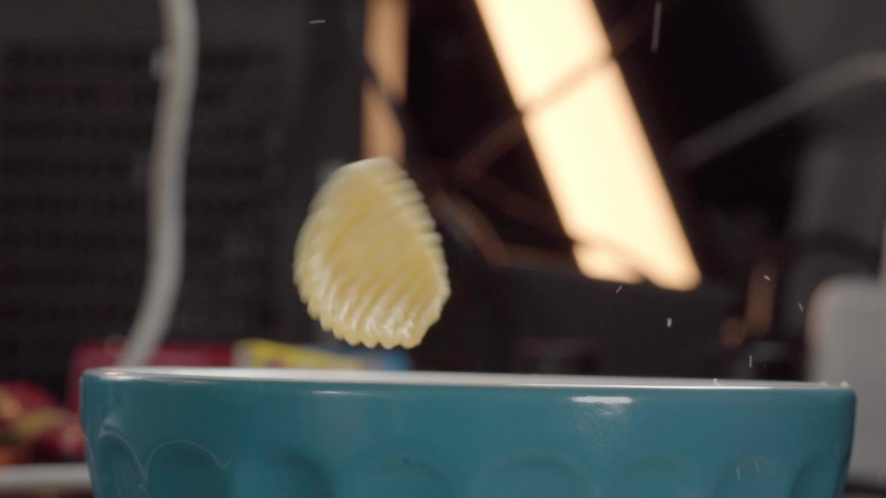Macro close up of ridged potato chips falling into a blue bowl, capturing crispy snack texture and motion with selective focus in an indoor kitchen environment.