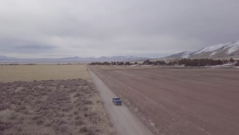 siguiendo a un camión mientras conduce por un camino de tierra en tierras de cultivo con colinas y montañas en la distancia - vista aérea