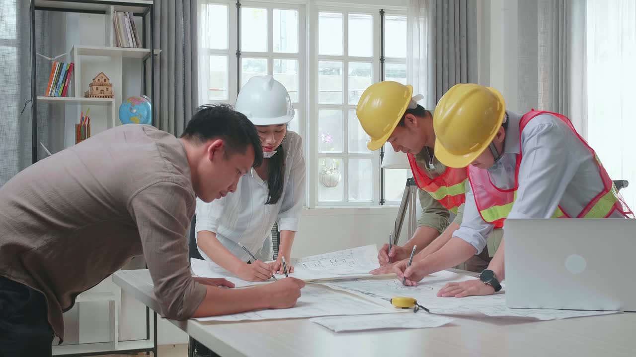 Three Asian Engineers With Helmets Helping A Man Drawing Building Construction At The Office