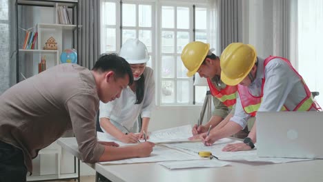 three asian engineers with helmets helping a man drawing building construction at the office