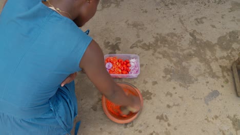 woman hands are grinding chili peppers and purple onions with a mortar to make sauce, a side dish of banku, in ghana