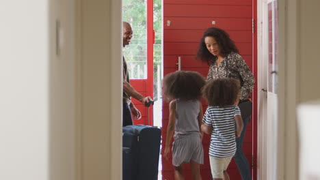 famiglia in piedi alla porta d'ingresso con una valigia che sta per partire in vacanza