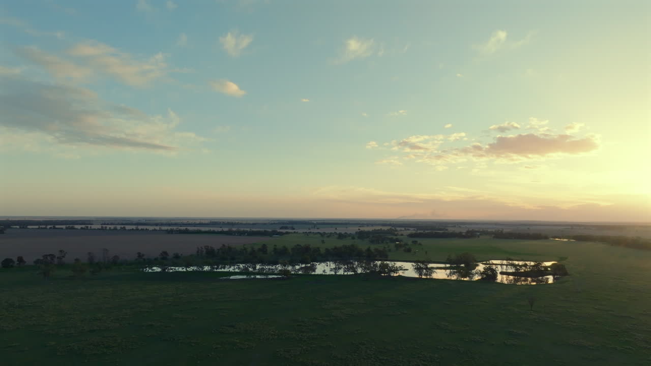 Aerial: Flying over fields towards a large dam reflecting shadows during the sunset, near Moree, Australia