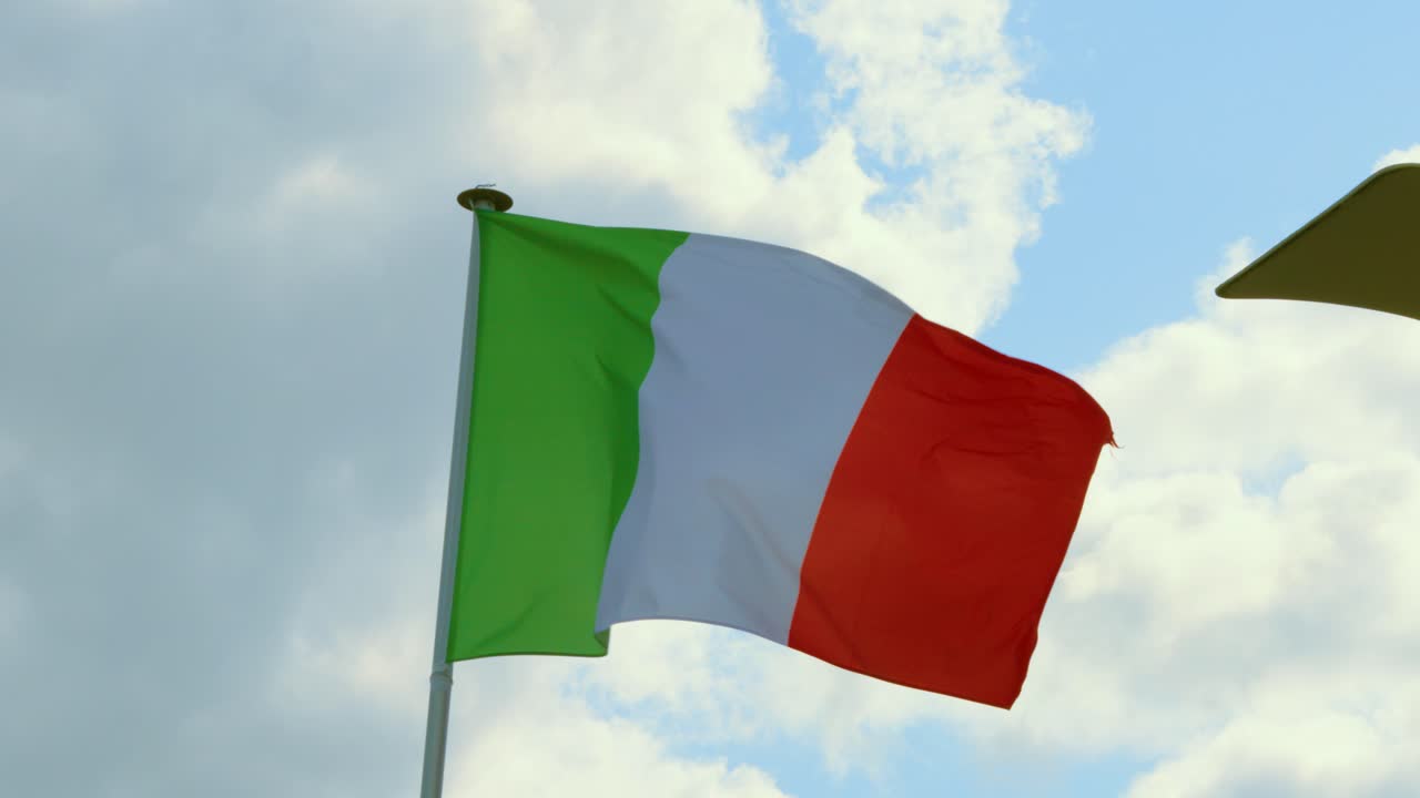 Bandiera italiana che sventola al vento al rallentatore con sfondo di cielo blu luminoso e nuvole.