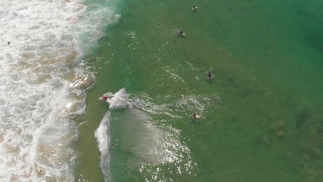 surfers riding on the perfect wave in the bright blue sea in algarve, portugal - aerial top-down panning shot