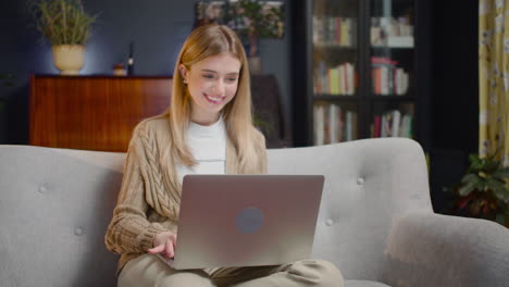 beautiful young woman chatting on laptop computer while sitting on couch at home