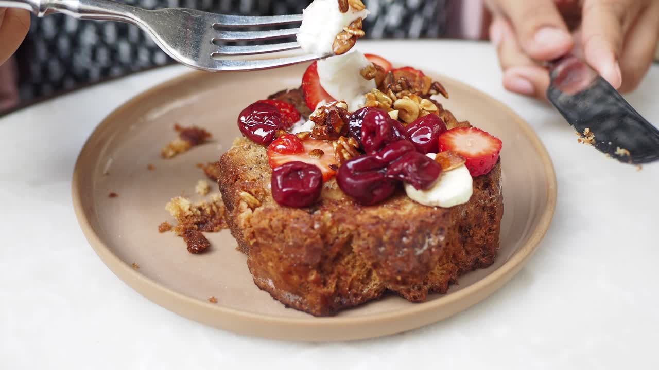 Close-up of a plate of banana bread with strawberries, cherries, whipped cream, and nuts