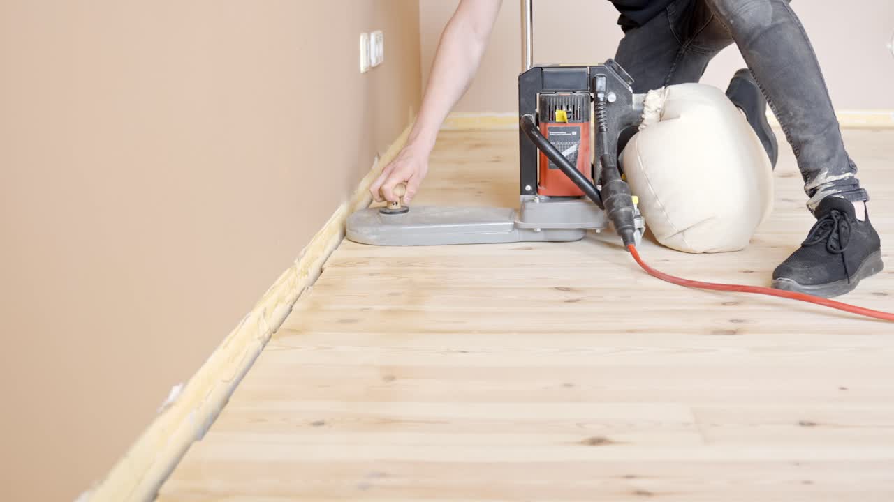 Worker Using Floor Sander In Refinishing Wooden Flooring, Polishing Edge By The Wall. side view, static shot