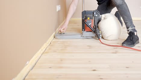 worker using floor sander in refinishing wooden flooring, polishing edge by the wall. side view, static shot