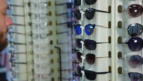 fashionable sunglasses on stand at optics. man testing new glasses in the shop. buyer choosing eyewear in optical store.