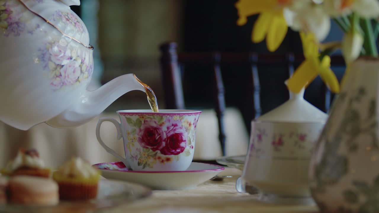 la tetera se vierte en la taza de té en una mesa bellamente colocada con flores y pasteles