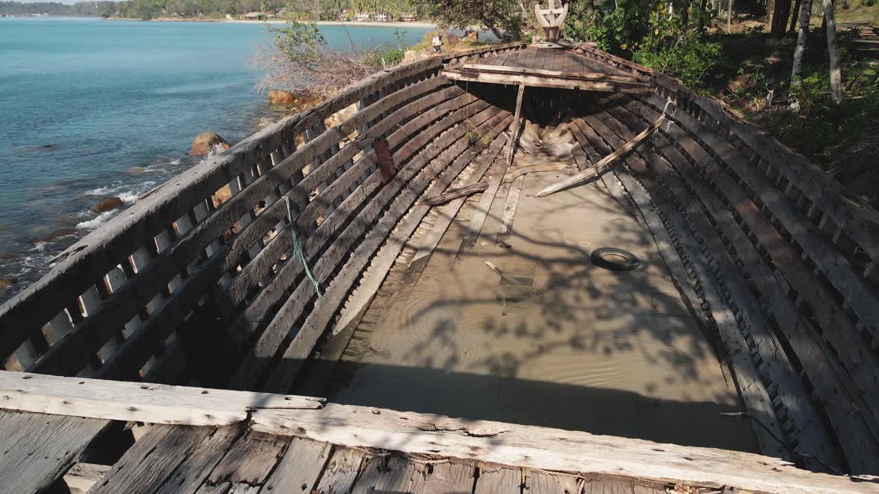 viejo barco de madera en la playa rocosa con playa de isla tropical en segundo plano.