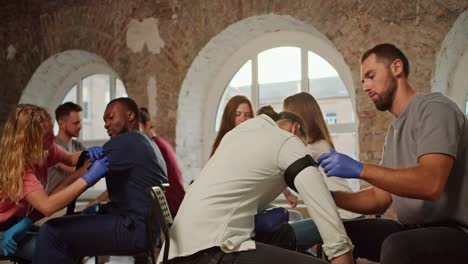 practical training of labor skills with medical harnesses. girl tightens medical tourniquet on hand of black male assistant in blue medical uniform