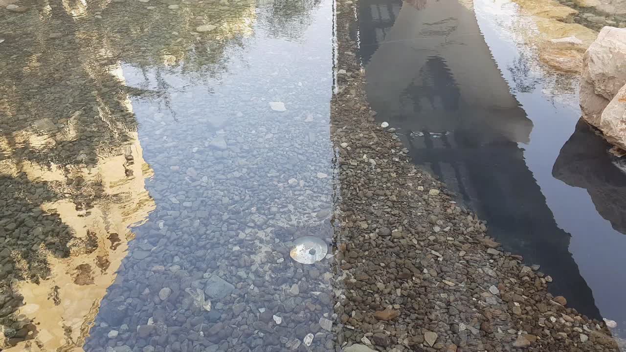 Stagno artificiale limpido con rocce di diverse dimensioni e colori, inclinazione della telecamera verso l'alto