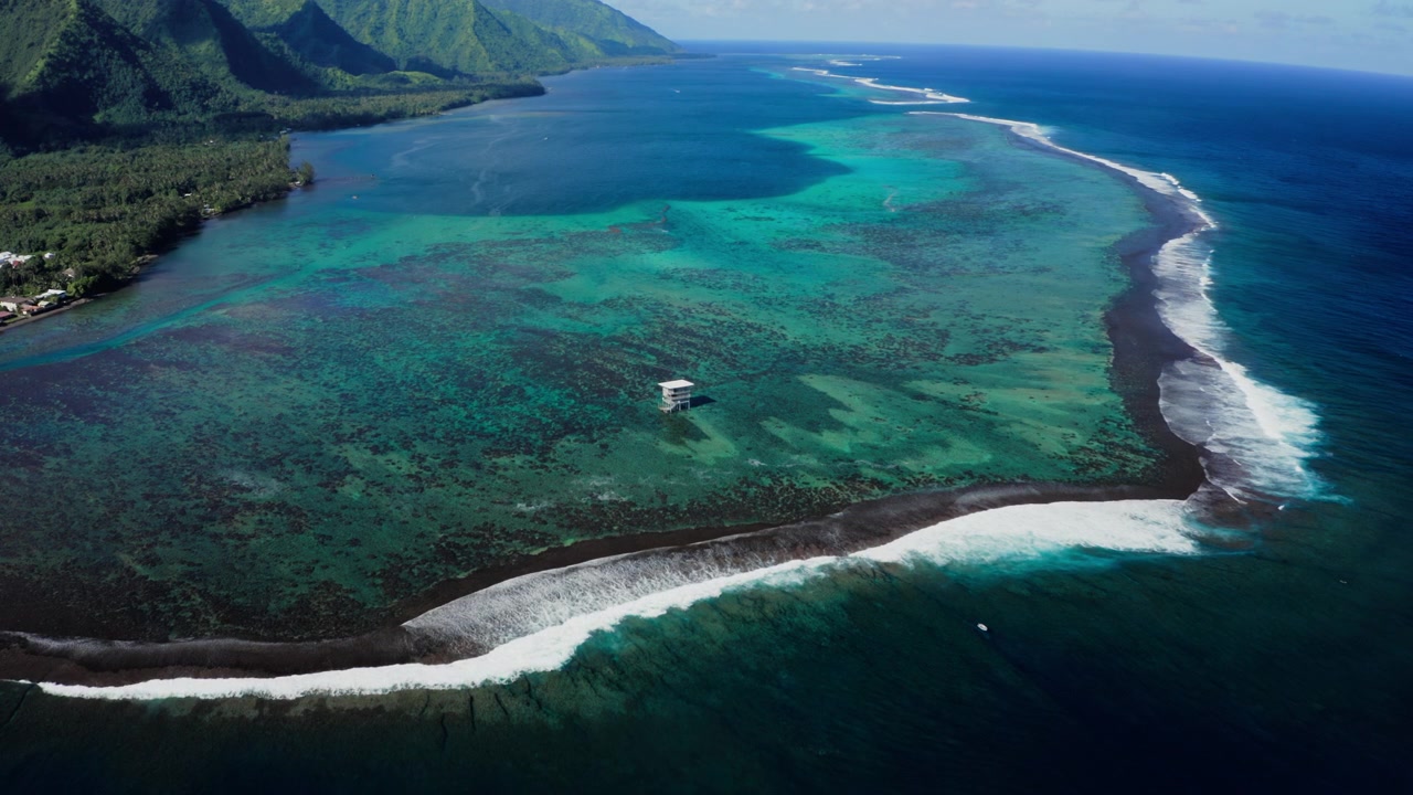 Vista aerea con drone della Torre dei Giudici di Teahupoo, Tahiti, barriera corallina e canale turchese incorniciati da montagne della foresta pluviale che si ergono sullo sfondo