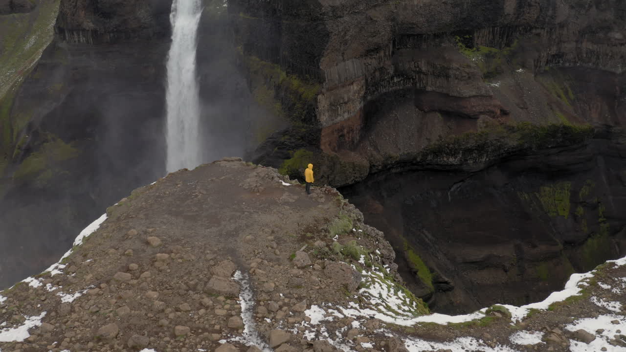 antena: toma panorámica lenta de un hombre parado cerca del borde de un acantilado, observando la cascada de haifoss en islandia