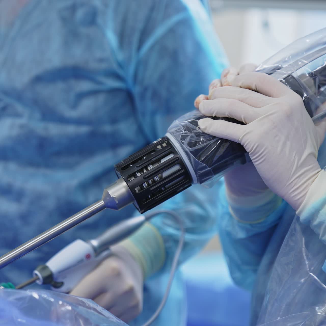 Modern technological devices used in operation. Assistant's hands holding heavy tool over the patient. Surgeon applies electronic equipment at backdrop in blur