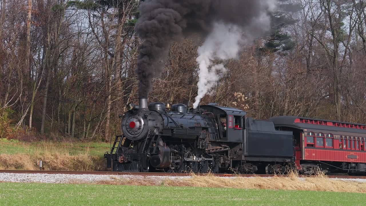 A classic steam engine chugs along the countryside, releasing plumes of smoke as it pulls a vintage passenger car past colorful autumn trees in a serene landscape.