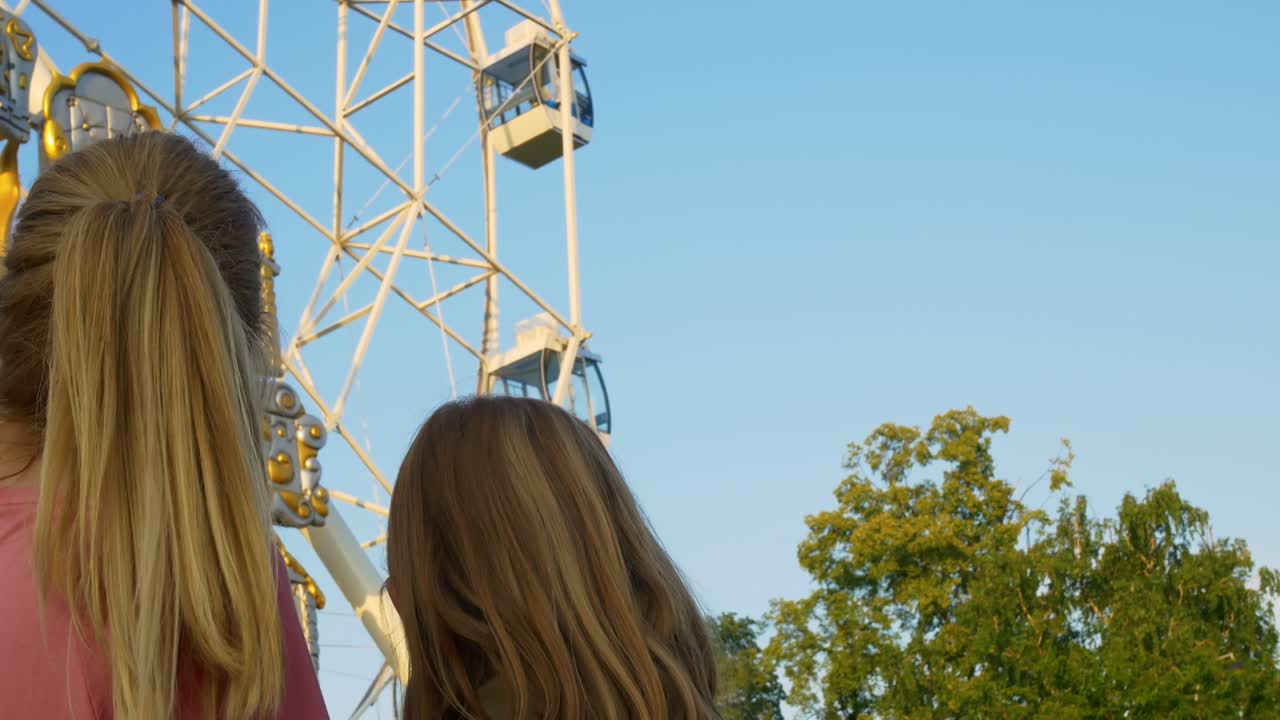 Mamma e figlia al parco divertimenti guardano la bellissima ruota panoramica, indicando le persone felici nelle cabine. Madre e figlia si divertono al luna park