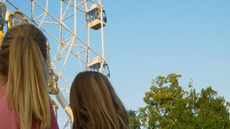 mom and daughter in the amusement park look at the beautiful ferris wheel, pointing at the happy people in the booths. mother and daughter are having fun at the fair