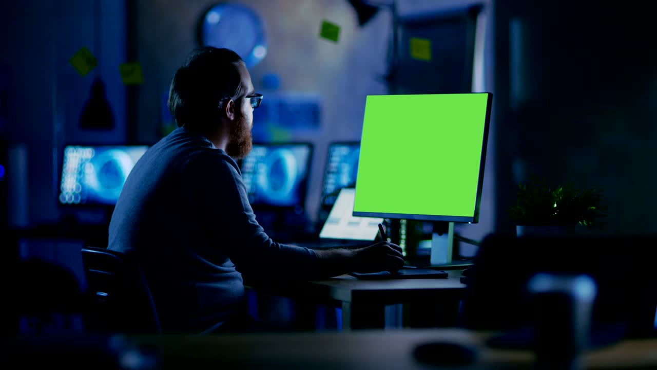 un hombre creativo con barba trabaja en una computadora personal con una pantalla verde aislada. trabaja solo en la oficina tarde en la noche.