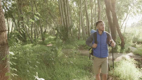 African-american-man-wearing-backpack-and-hiking-with-trekking-poles-in-forest,-slow-motion