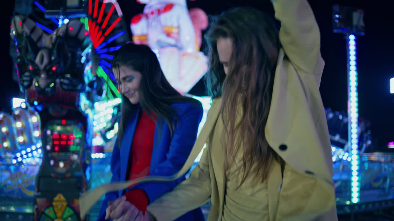 Happy girls dancing city amusement park at night. Cheerful girlfriends weekend