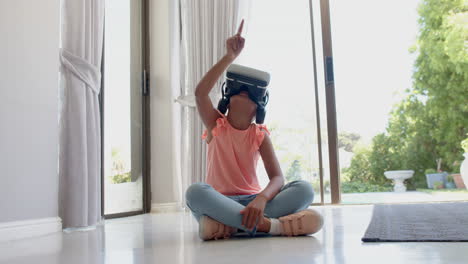 una chica biracial feliz usando auriculares vr usando una interfaz virtual en casa, en cámara lenta