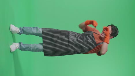 full body of cheerful asian male housekeeper with an apron dancing while standing in the green screen studio