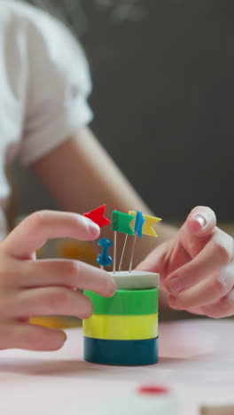 little schoolgirl puts eraser with tag pins on plastic rings at workplace in classroom closeup. girl makes castle of stationery in school playroom