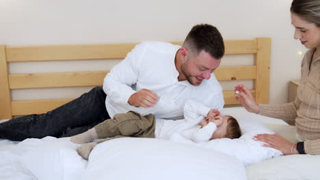 dad waves his little baby boy and puts him on the pillows. mother touches hair of her beloved son.