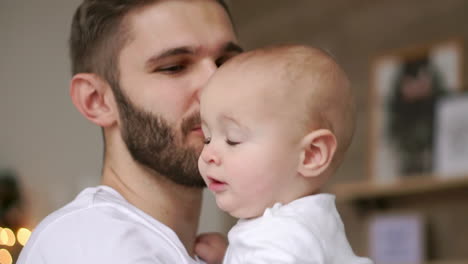 Bearded-dad-kissing-baby.-Close-up-of-happy-father-with-child-on-hands.-Baby-touching-wrist-watch-on-father-hand.