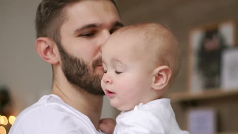 Papá-Barbudo-Besando-Al-Bebé.-Cerca-De-Un-Padre-Feliz-Con-Un-Niño-En-Las-Manos.-Bebé-Tocando-El-Reloj-De-Pulsera-En-La-Mano-Del-Padre.