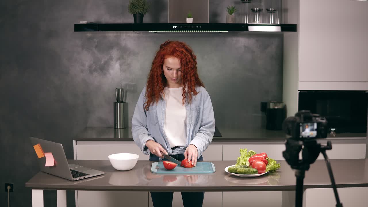 una mujer joven con ropa casual dirige un blog culinario y graba video en la cocina gris. video de rodaje del blog - pelirroja