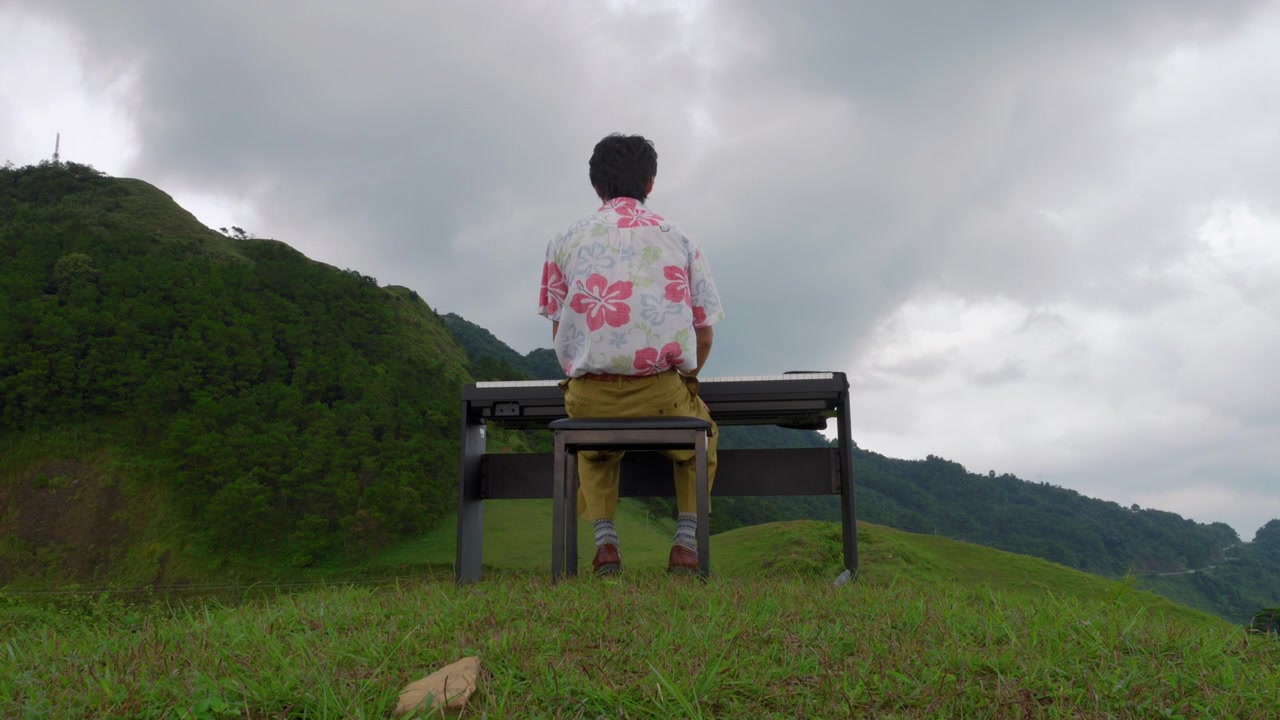 演奏前に、熱帯の山岳風景を望むピアノのベンチに座る演奏者の後ろ姿。