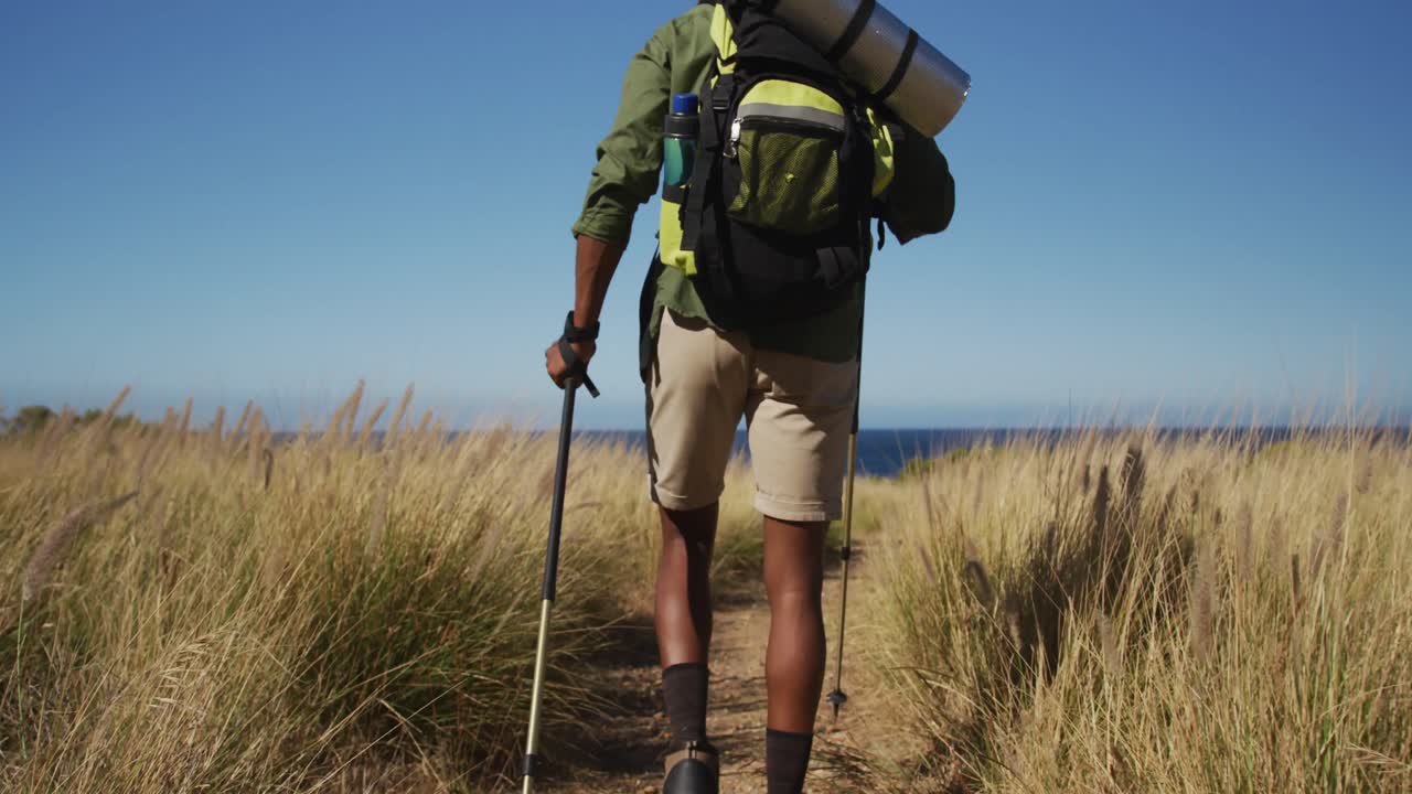 hombre afroamericano haciendo senderismo con palos de senderismo en el campo por la costa