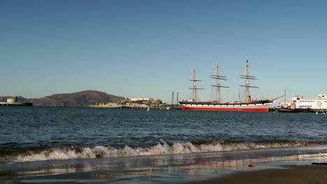 california beach with waves and historic sail boat on the ocean