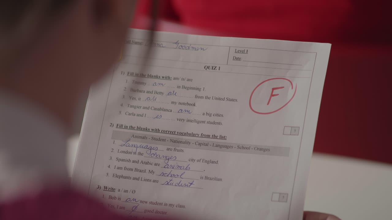 Et over-skulder-skud viser en studerende, der holder en skoleprøve med et stort rødt F for fiasko. Et koncept om dårlige karakterer, akademisk stress og uddannelsesmæssig skuffelse.
